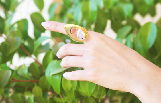woman hand wearing a big gold ring - green nature leaves background
