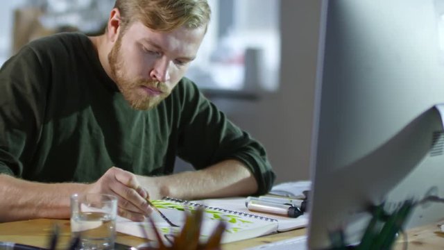 Medium shot of male illustrator dipping brush in water and pre-wetting paper in his sketchbook before painting