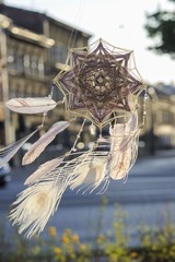 Handmade mandala God's Eye dream catcher with white peacock feathers and amethyst crystals on city background in Krakow
