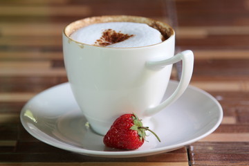 A cup of hot coffee with strawberry on white saucer.