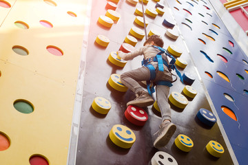 The stronger you climb, the higher your pedestal! Small child boy as an alpinist climbing the wall in the play room for children.