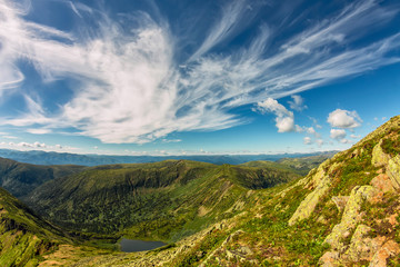Lake in green mountains with feathery clouds, summer landscape