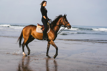 side view of young woman riding horse with ocean behind