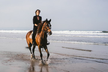 young woman riding horse with wavy ocean behind