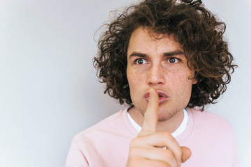 Closeup portrait of serious male with trendy curly hairdo, keeps fore finger on lips, tries to keep...