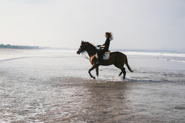 young female equestrian riding horse in water