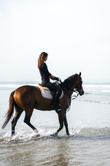 Fototapeta na wymiar side view of young female equestrian riding horse in water