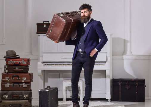 Man, traveller with beard and mustache with baggage, luxury white interior background. Macho stylish on strict face stands and carries big vintage suitcase. Baggage and travelling concept.