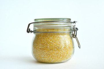 Yellow corn groats in a glass jar on a white background