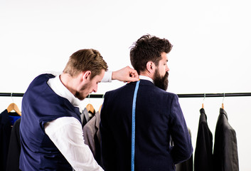 Businessman, client stand near hanger with suits while tailor working.