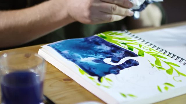 Close up hands of unrecognizable male illustrator pressing paper tissue against painting to remove extra liquid from it