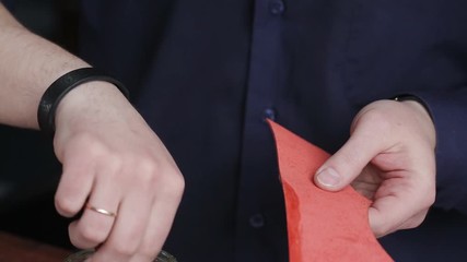 Leathersmith is applying glue on a leather parts of the zipper with a special brush. He works at the table in the workshop.