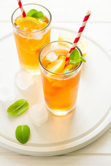 Glasses of iced tea with lemon slices and mint on white wooden background