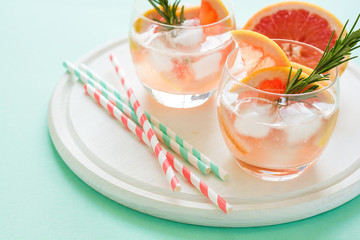 Refreshment grapefruit cocktail with rosemary on white wooden board. Healthy citrus summer drink. Mint color background