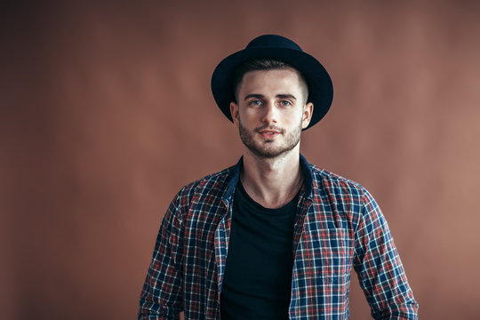 Young handsome hipster man in hat posing on brown background
