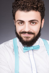 Portrait of stylish young man in white shirt and bow tie. Curly dark hair, beard and mustache
