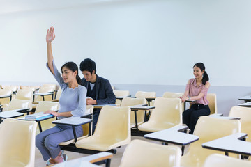 Young woman and friend student raising hands in a classroom showing ready answer. concept of education.