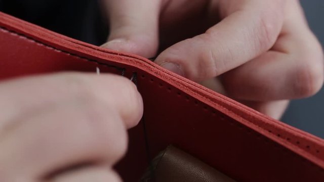 Man creates a brown leather wallet with his own hands with a needle in the leather workshop, closeup
