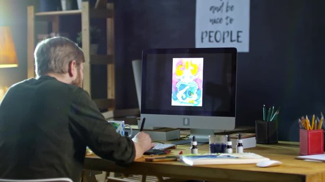 Rear view of male illustrator working with drawing tablet connected to computer to create picture of fantasy creature