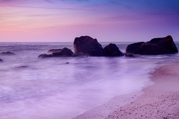 Fototapeta na wymiar Summer seasonal natural vacation background. Romantic morning at sea. Big boulders sticking out from smooth wavy sea. Pink horizon with first hot sun rays. Long exposure.