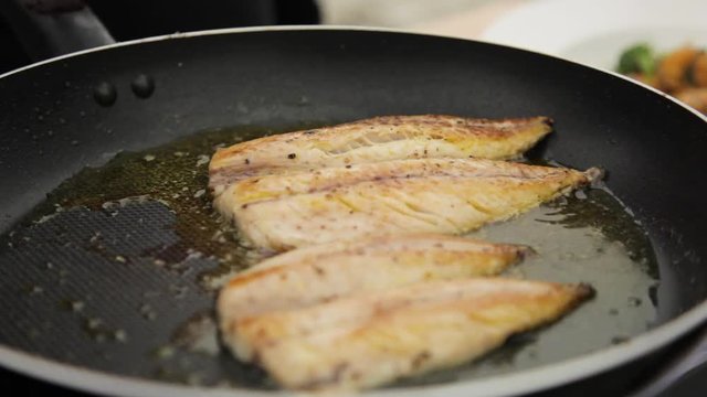 A medium shot of two fish beng fried in a pan