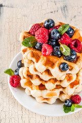 Belgian waffles with raspberries, blueberries and syrup, homemade healthy breakfast, light concrete background copy space