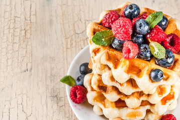 Belgian waffles with raspberries, blueberries and syrup, homemade healthy breakfast, light concrete background copy space