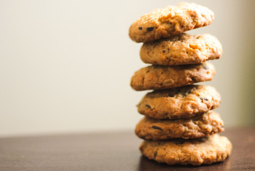Shiny pile of golden brown homemade oatmeal cookies on dark table background. High tower of tasty redden oatcakes, healthy sweet home-baked products
