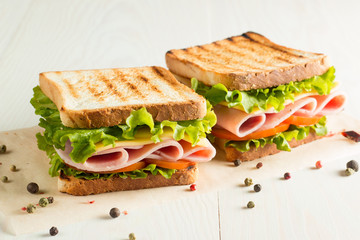 Close-up photo of a club sandwich. Sandwich with meet, prosciutto, salami, salad, vegetables, lettuce, tomato, onion and mustard on a fresh sliced rye bread on wooden background. Olives background.