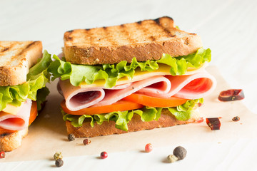 Close-up photo of a club sandwich. Sandwich with meet, prosciutto, salami, salad, vegetables, lettuce, tomato, onion and mustard on a fresh sliced rye bread on wooden background. Olives background.