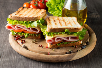 Close-up photo of a club sandwich. Sandwich with meet, prosciutto, salami, salad, vegetables, lettuce, tomato, onion and mustard on a fresh sliced rye bread on wooden background. Olives background.
