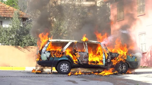 A fire destroys a car in the street.
