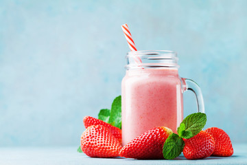 Pink strawberry smoothie or milkshake in mason jar on blue table. Healthy food for breakfast and snack.