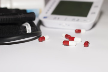 Blood pressure monitor on white background with tablets