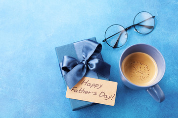 Morning cup of coffee, gift box and eyeglasses on blue table for breakfast on Happy Fathers Day.