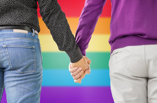 same-sex relationships, lgbt and homosexual concept - close up of male gay couple holding hands over rainbow background