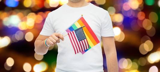 lgbt, same-sex relationships and homosexual concept - close up of man wearing gay pride rainbow awareness wristband and holding american flag over lights background