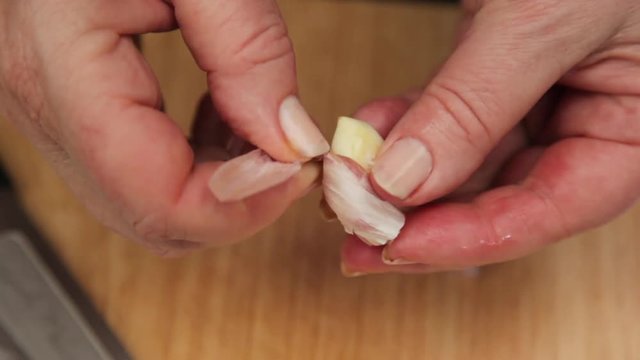 A close up shot of a garlic being crushed using a knife.