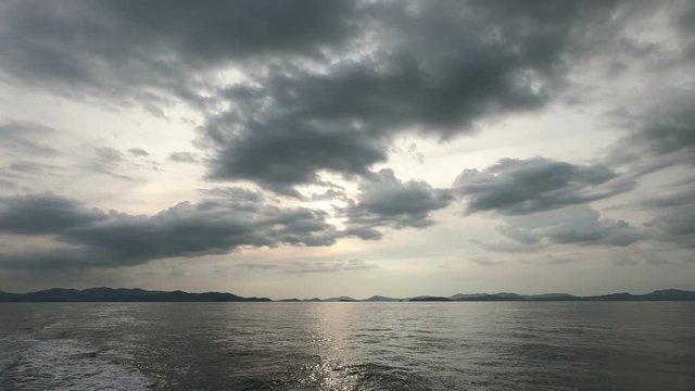 Sea wide shot on the boat with land on the horizon in far distance during and clouds