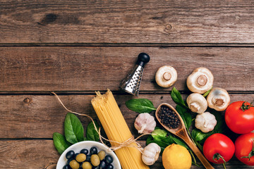 Pasta ingredients - tomatoes, olive oil, garlic, italian herbs, fresh basil, salt and spaghetti on a wooden background with copy space, horizontal, top view