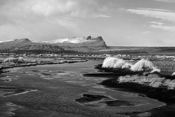 Autumn landscape in Iceland in black and white with a river, black sand and dry grass in foreground