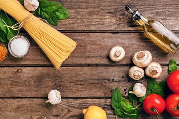 Pasta ingredients - tomatoes, olive oil, garlic, italian herbs, fresh basil, salt and spaghetti on a wooden background with copy space, horizontal, top view