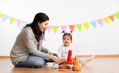 family, holidays and people concept - happy mother and little daughter playing with ring pyramid baby toy on birthday party