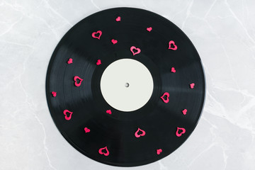 Vinyl record covered with red hearts on a marble background.