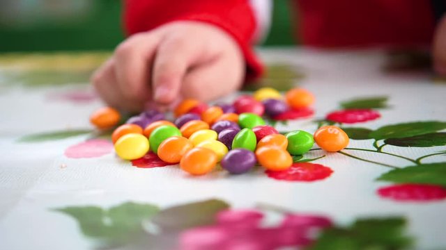 Little colored candy. Child hands takes candy from the table.