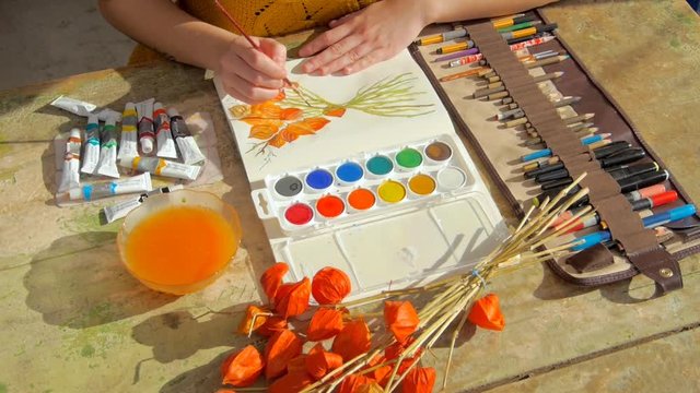 young female artist painting a picture of a red physalis plant in front of her