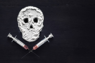 Narcotic powder in the form of a skull and syringes with injection. Copy space. The concept of addiction kills.