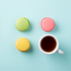 Cup of tea with colorful macarons on light blue background
