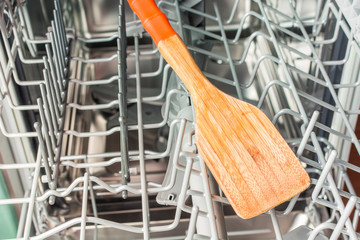 Yellow wooden spatula lies in the middle of the dishwasher compartment