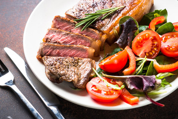 Grilled beef striploin steak with salad in plate.